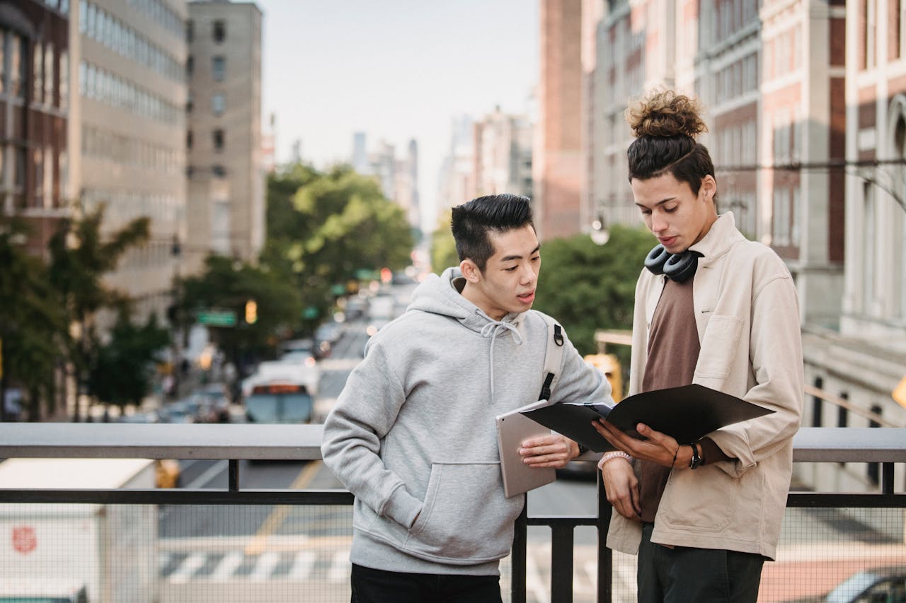 Two young men reviewing documents on an urban bridge, focused on learning and collaboration.