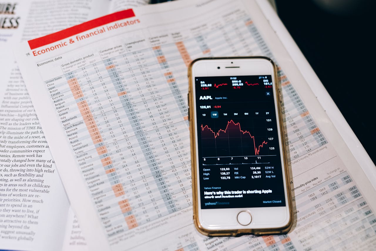 About Smartphone displaying stock market data on papers with financial charts.